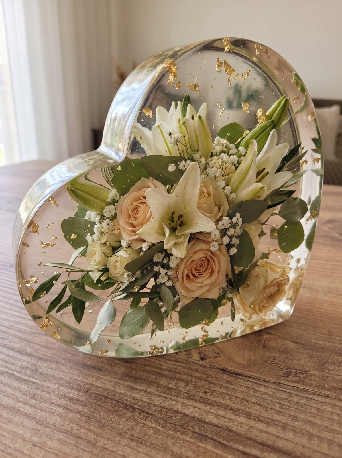 Peça em resina em forma de coração com as rosas cor de pêssego, os lírios, a gipsófila e o eucalipto do bouquet, com folha de ouro
